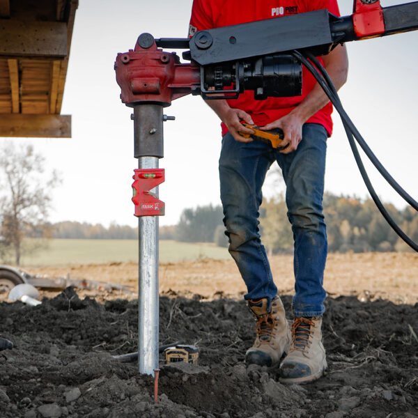 Installer standing beside a screw pile, operating the boom and drive head by remote control