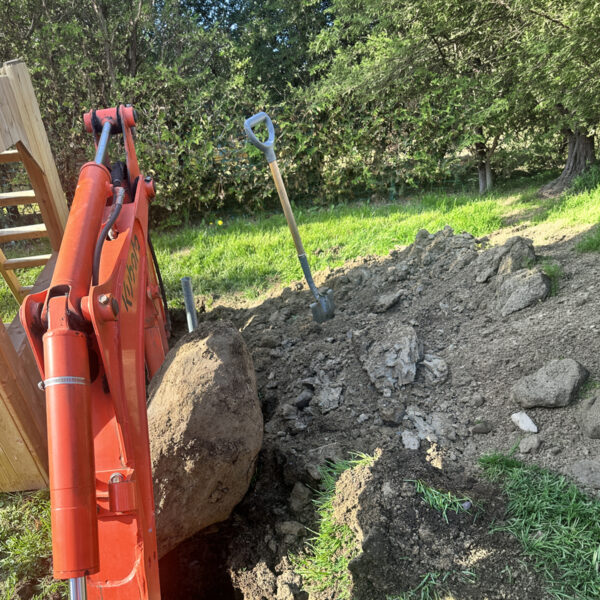 ractor with a built-in backhoe clearing an obstacle before installing a screw pile